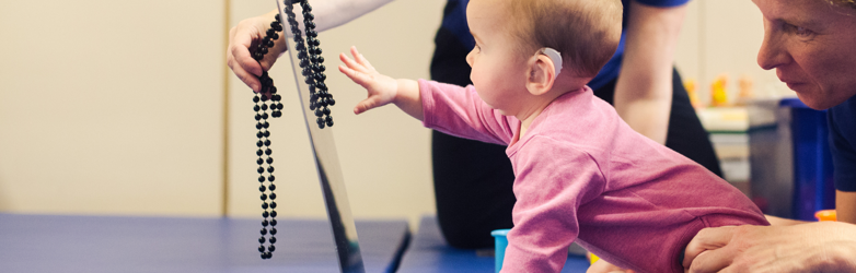 baby girl reaching out to grab beads whilst a therapist holds her legs 