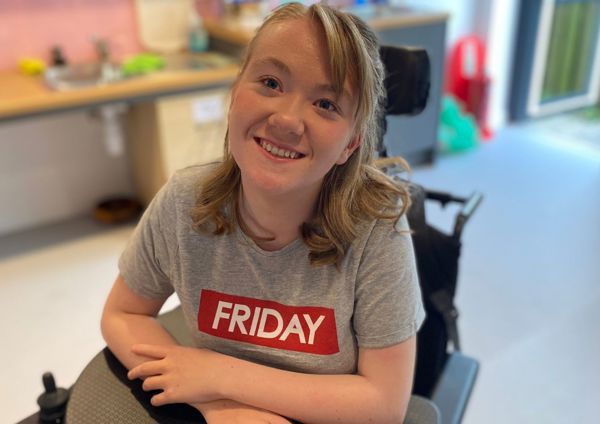 Photograph of teenage girl sitting in wheelchair, smiling up at camera.