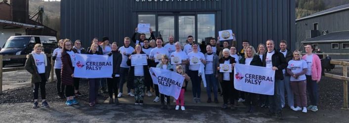 Photograph of group of people in Cerebral Palsy Cymru t-shirts, holding branded signs at Zipworld in Aberdare. 