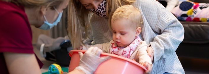 Therapist holding up therapy toy for a baby who is being supported by her mother.