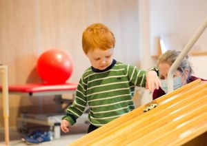 Older child in therapy, placing a toy car on a ramp.