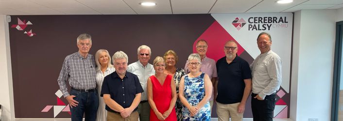 Photograph of founding parents standing in front of Cerebral Palsy Cymru branded wall in the centre. 