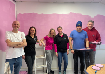 Group of volunteers holding paint supplies in front of a freshly painted pink wall